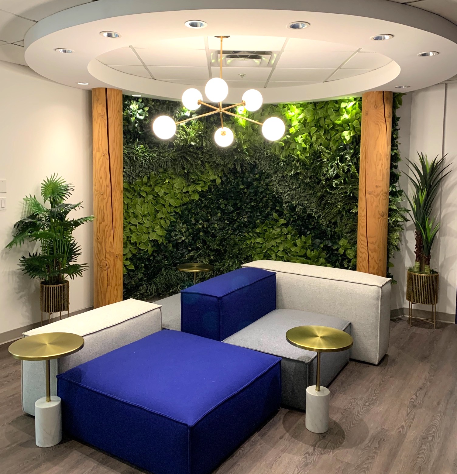 Artificial green wall behind a lounge seating area with artificial potted tropical plants.