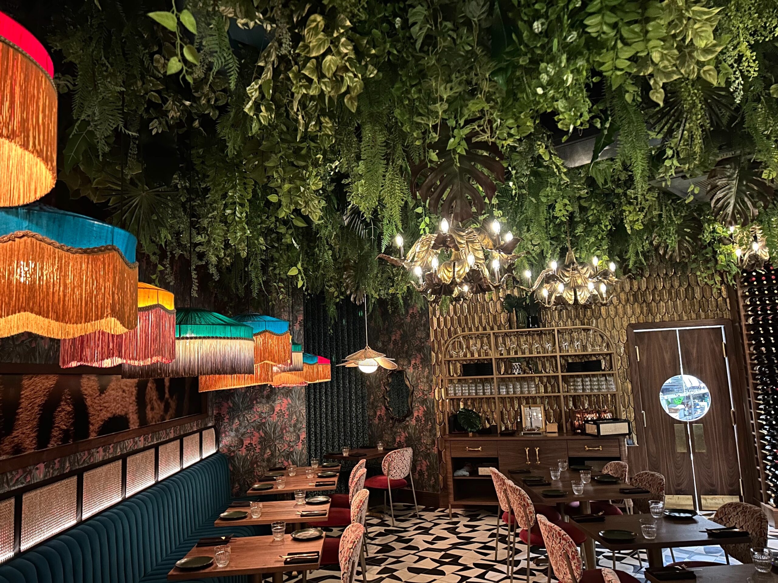 Restaurant interior with artificial ceiling greenery and colourful vintage pendant lighting.